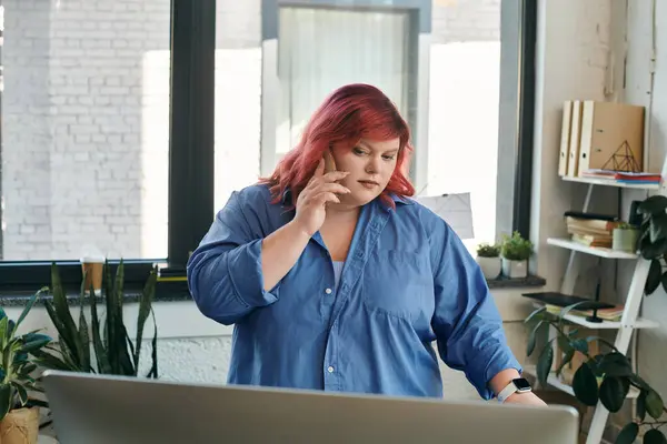 Uma mulher plus size com cabelo rosa fica em sua mesa falando ao telefone. — Fotografia de Stock