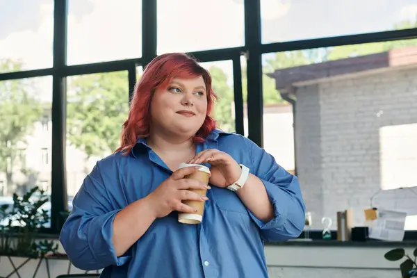 Una donna d'affari plus size con capelli rossi vibranti gode di una tazza di caffè da una finestra. — Foto stock
