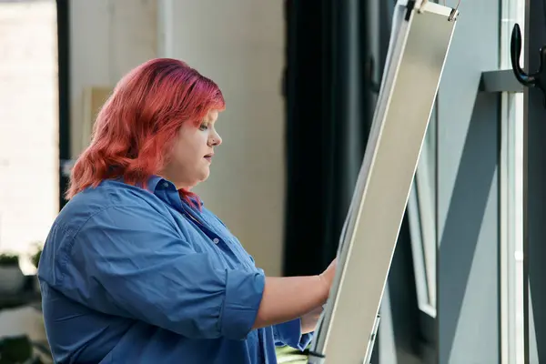 A plus size woman with vibrant pink hair adjusts a blank canvas. — Stock Photo