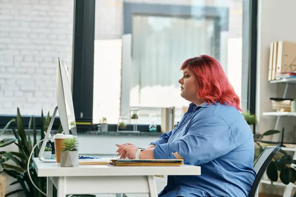 Une femme de taille plus avec les cheveux roses travaille sur un ordinateur dans un cadre de bureau. — Photo de stock