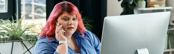 A plus size businesswoman with pink hair on the phone while looking at a computer screen. — Stock Photo