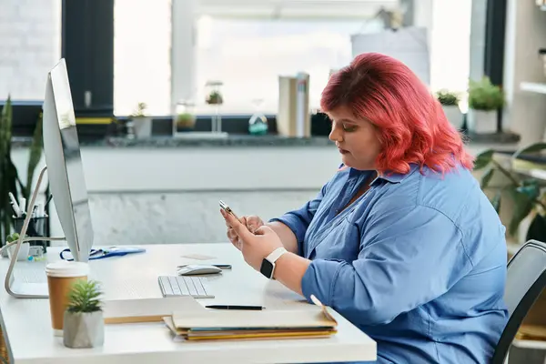 A plus size businesswoman with pink hair sits at her desk, checking her phone. — Stock Photo