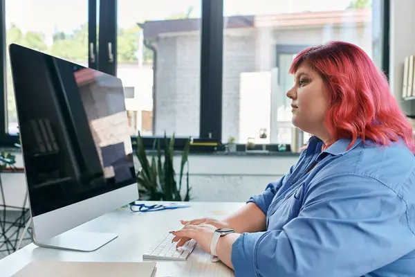 Uma mulher de negócios plus size senta-se numa secretária, a escrever num computador.. — Fotografia de Stock