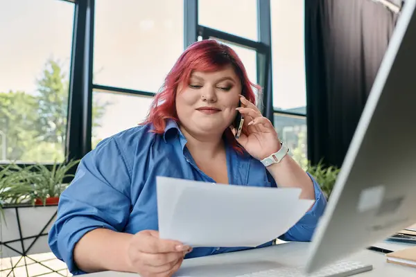 Une femme de taille plus est sur un appel téléphonique, l'examen des documents à son bureau. — Photo de stock