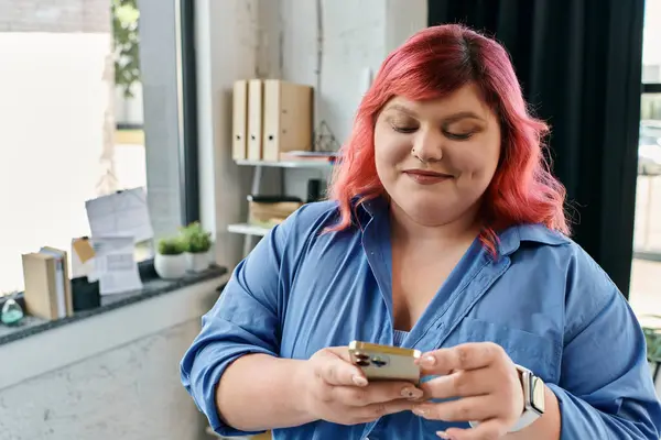 A plus size woman with pink hair checks her phone in a modern office space. — Stock Photo
