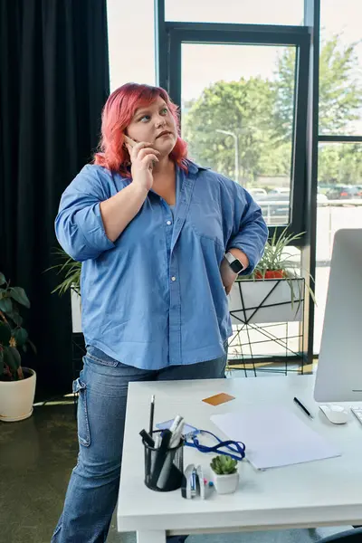 Une femme de taille plus avec les cheveux roses parle sur un téléphone tout en se tenant près d'un bureau dans un cadre de bureau moderne. — Photo de stock