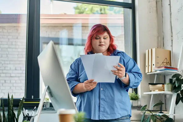 Женщина plus-size с рыжими волосами внимательно читает документы, ее выражение сосредоточено. — стоковое фото
