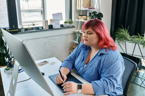 Una mujer de talla grande con el pelo rosado vibrante trabaja en un diseño digital con un lápiz óptico y una tableta. - foto de stock