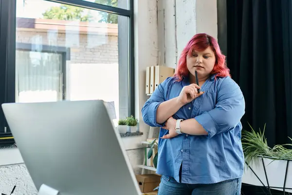 A plus size woman in a blue shirt and jeans ponders a thought while standing by a window in an office. — Stock Photo