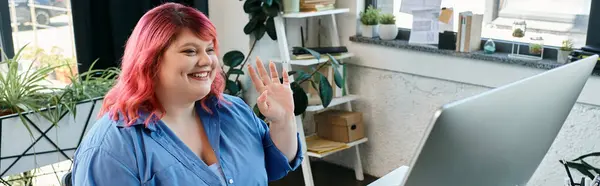 A plus size woman with pink hair smiles and waves while video chatting. — Stock Photo