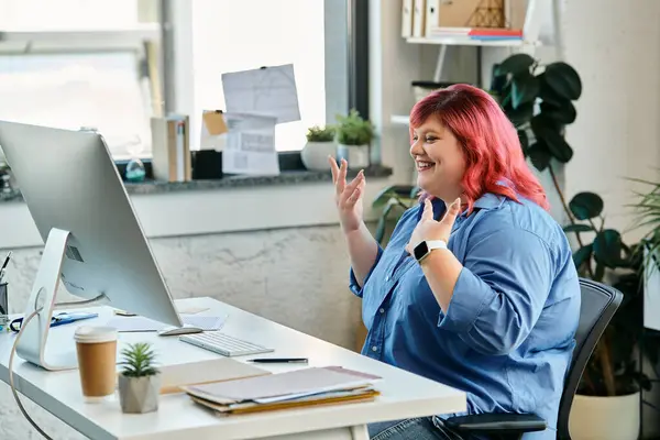 Женщина plus-size с рыжими волосами возбужденно жестикулирует во время видеозвонка у своего стола. — стоковое фото