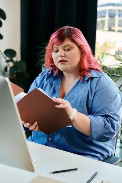 Plus size woman with pink hair reviews a document at her desk. — Stock Photo