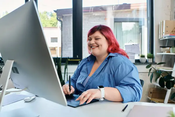 A plus size woman with vibrant red hair smiles while working on her computer. — Stock Photo