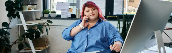 A plus size woman works at a computer, talking on the phone. — Stock Photo
