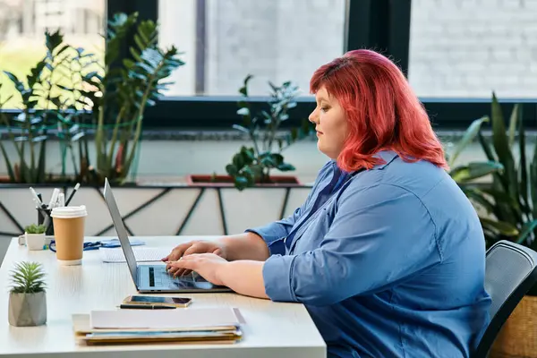 Eine Plus-Size-Frau tippt auf einem Laptop am Schreibtisch, umgeben von lebendigen Pflanzen. — Stockfoto