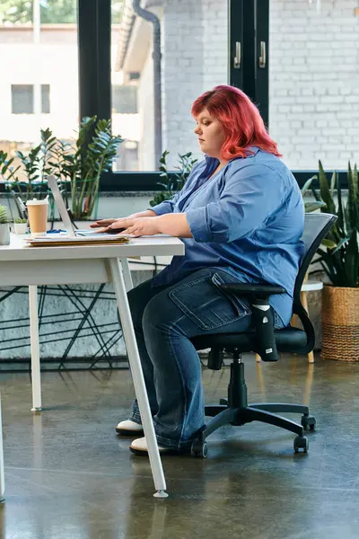Mujer de tamaño grande con pelo rosa trabaja en el escritorio blanco en la oficina moderna en el ordenador portátil - foto de stock