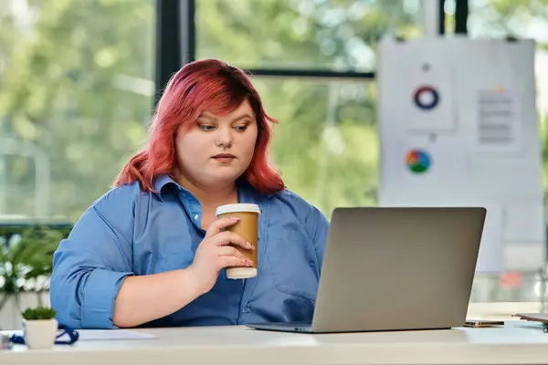 A plus size woman sits at a desk, concentrating on her laptop while holding a cup of coffee. — Stock Photo