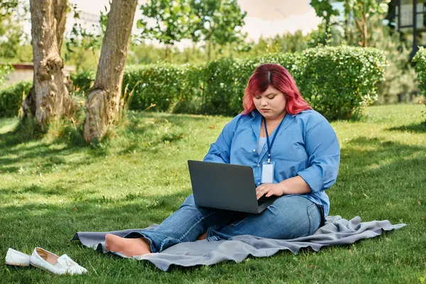 Женщина plus size в яркой мантии сидит на одеяле в парке, работая на ноутбуке. — Stock Photo