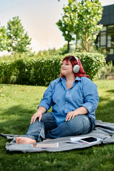 Una donna plus size siede su una coperta in un parco, indossando cuffie e godersi il sole. — Stock Photo