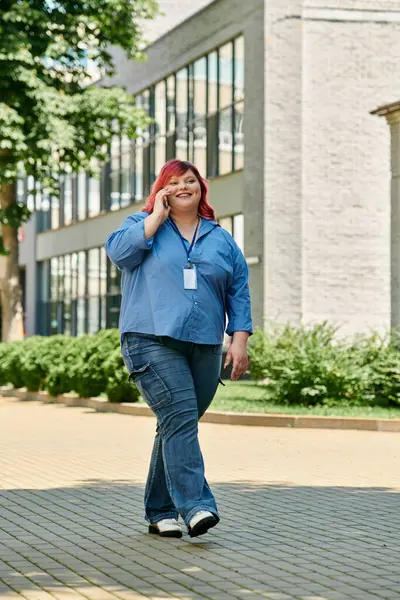 A plus size woman with pink hair walks down a city street, talking on her phone with a big smile. — Stock Photo