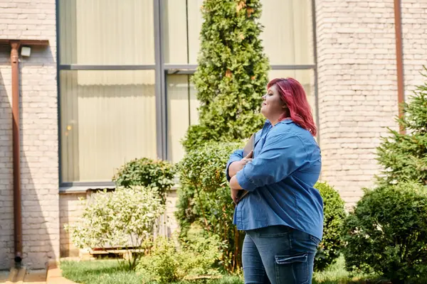 Женщина plus-size с рыжими волосами и буйным чердаком прогуливается по освещенному солнцем двору. — стоковое фото