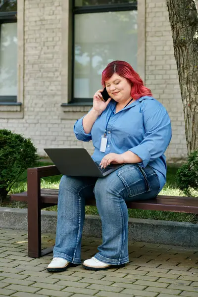 Женщина plus size сидит на скамейке, используя ноутбук и телефон. — стоковое фото