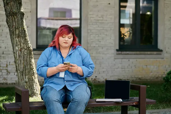 A plus size woman in blue shirt and jeans sits on bench outdoors, looking at phone — Stock Photo
