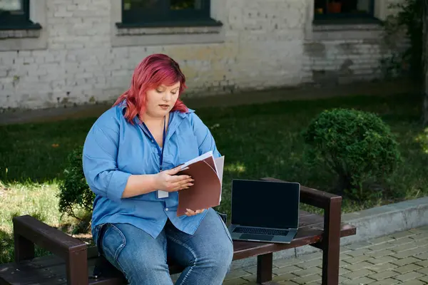 Женщина plus size сидит на скамейке, изучая бумаги с ноутбуком рядом. — стоковое фото