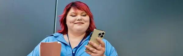 A plus size woman with bright red hair smiles as she checks her smartphone. — Stock Photo