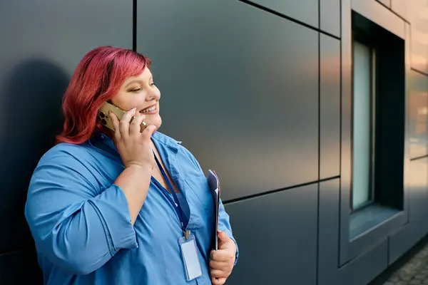 Женщина plus-size с розовыми волосами улыбается, когда говорит по телефону в городской обстановке. — стоковое фото