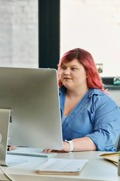 Pink-haired plus size woman in blue shirt, working at computer desk — Stock Photo