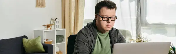Человек с синдромом Дауна сосредоточен на ноутбуке в уютной, хорошо освещенной комнате.. — стоковое фото