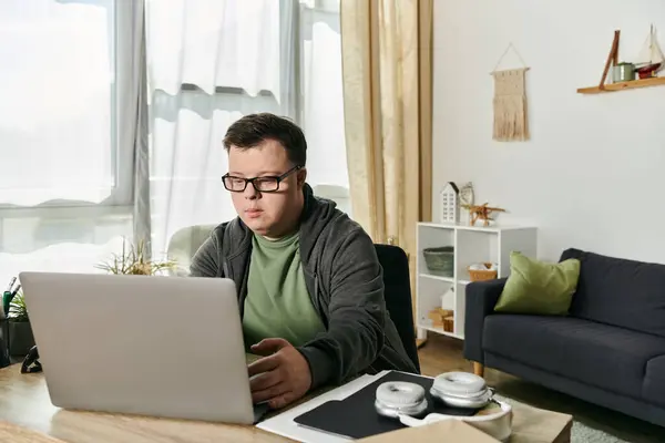 A young man with Down syndrome focuses intently on his laptop. — Stock Photo