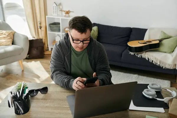 A man with Down syndrome engages with his smartphone while sitting at a desk. — Stock Photo