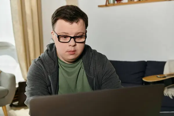 A young man with Down syndrome engages with his laptop in a cozy home setting. — Stock Photo
