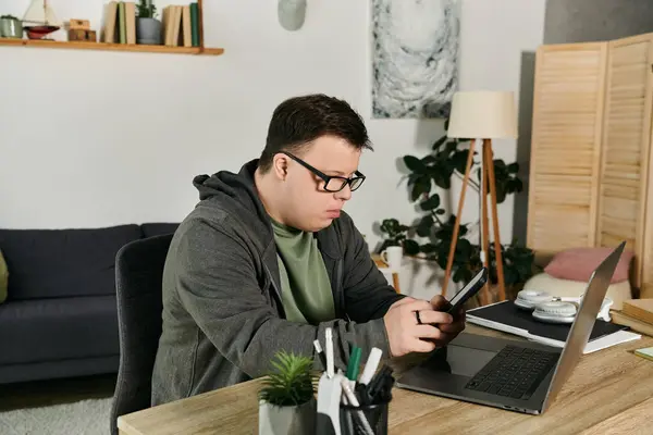 A young man with Down syndrome engages with his phone while seated at a desk. — Stock Photo