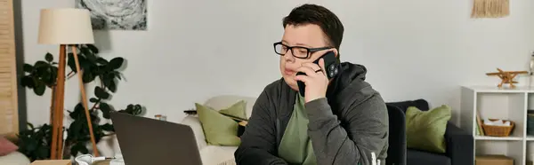 Un giovane con la sindrome di Down parla al telefono mentre è seduto alla sua scrivania. — Foto stock