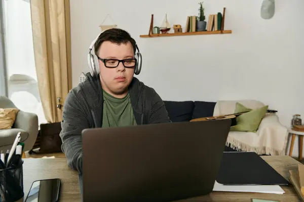 Man with Down syndrome wearing headphones focused on his laptop in a comfortable living area. — Stock Photo