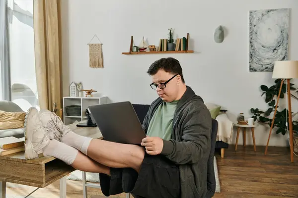 A man with Down syndrome sits comfortably at home, focused on his laptop. — Stock Photo