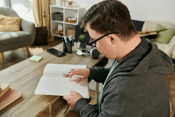 A man with Down syndrome explores the pages of a book in his cozy living space. — Stock Photo