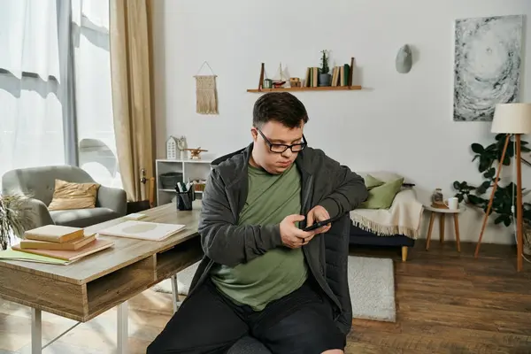 Un hombre con síndrome de Down utiliza su teléfono inteligente mientras está sentado cómodamente en casa. - foto de stock