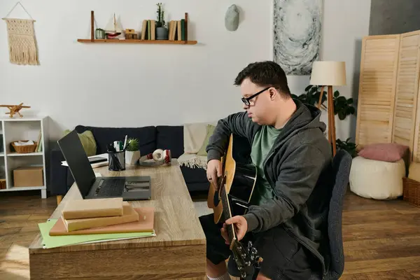 A young man with Down syndrome plays guitar at home, immersed in music and creativity. — Stock Photo