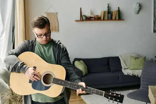 A young man with Down syndrome joyfully strumming his guitar in a warm, inviting living space. — Stock Photo
