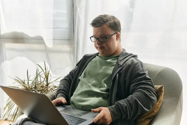 A young man with Down syndrome enjoys browsing on his laptop in a bright, comfortable living room. — Stock Photo