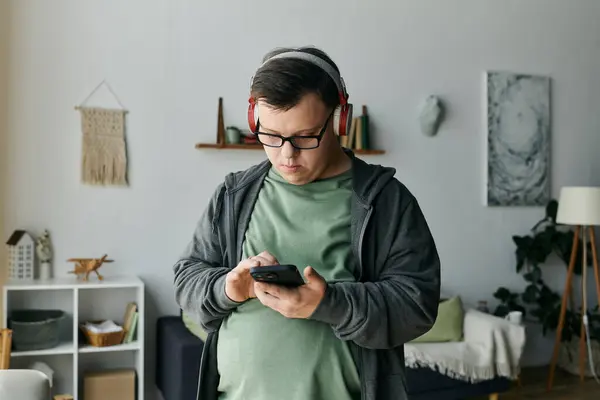 A young man with Down syndrome listens to music while focused on his smartphone. — Stock Photo