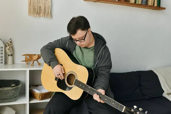A young man with Down syndrome plays guitar, enjoying a moment of creativity in his home. — Stock Photo