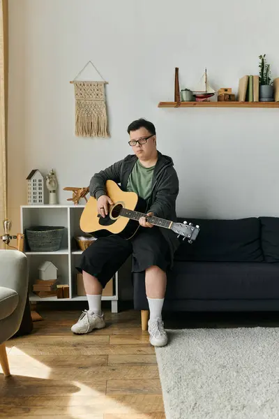A young man with Down syndrome enjoys playing guitar in his cozy home. — Stock Photo