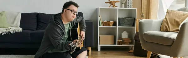 A man with Down syndrome enjoys strumming his guitar in a cozy living space. — Stock Photo