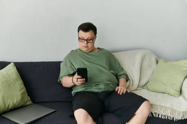 A man with Down syndrome enjoys leisure time at home, engaged with his smartphone. — Stock Photo