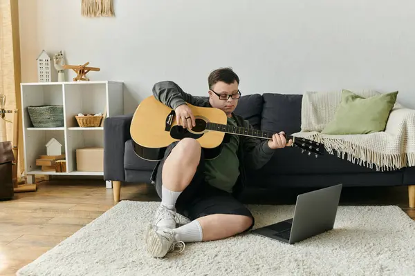 A young man with Down syndrome strums his guitar while seated on the floor. — Stock Photo